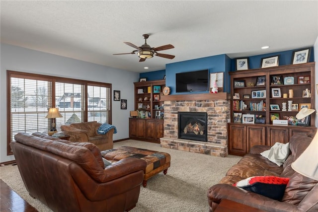 living room with a textured ceiling, ceiling fan, carpet floors, and a stone fireplace