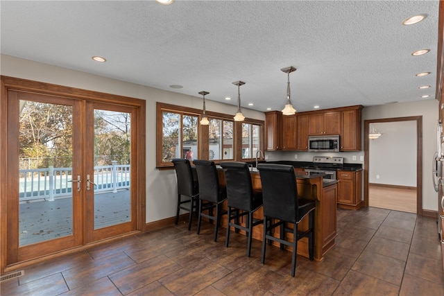 kitchen with a textured ceiling, a breakfast bar, stainless steel appliances, and decorative light fixtures