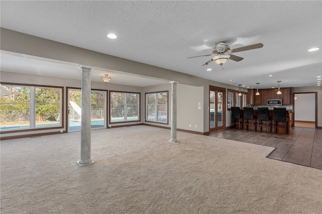 unfurnished living room with dark colored carpet, a textured ceiling, plenty of natural light, and ceiling fan