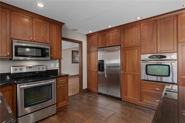 kitchen featuring a textured ceiling, appliances with stainless steel finishes, and dark stone counters