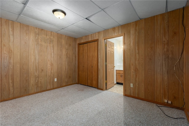 carpeted spare room with a paneled ceiling and wood walls