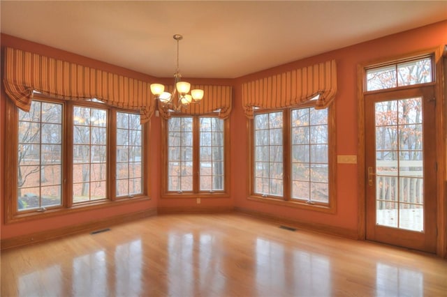 unfurnished dining area with baseboards, a healthy amount of sunlight, visible vents, and an inviting chandelier