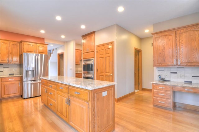 kitchen with recessed lighting, light wood-style flooring, appliances with stainless steel finishes, a kitchen island, and light stone countertops