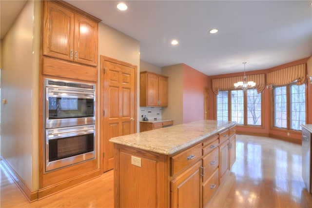 kitchen featuring double oven, light stone counters, light wood-type flooring, backsplash, and a center island