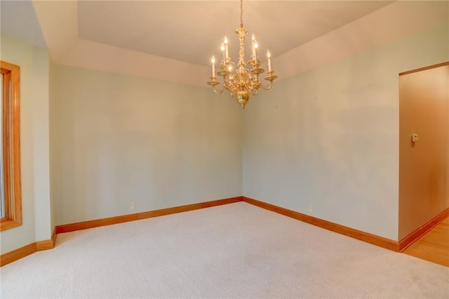 carpeted empty room featuring a chandelier and baseboards