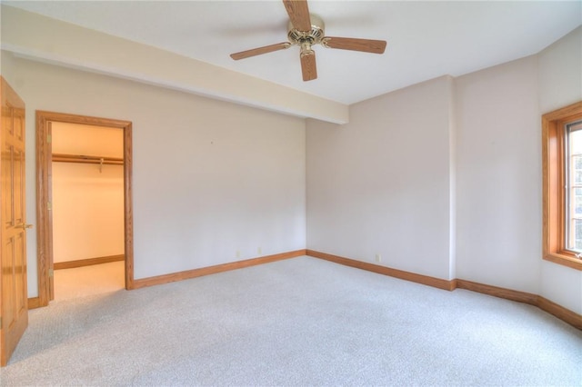 unfurnished bedroom featuring light colored carpet, ceiling fan, a spacious closet, and baseboards