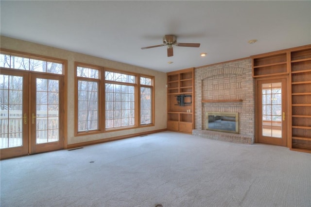 unfurnished living room with carpet floors, visible vents, built in features, french doors, and a brick fireplace