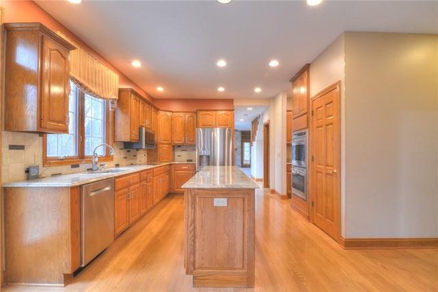 kitchen featuring tasteful backsplash, light wood-style flooring, a kitchen island, appliances with stainless steel finishes, and a sink