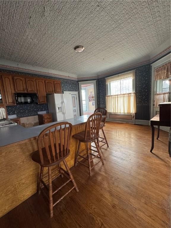 kitchen with crown molding, white refrigerator with ice dispenser, a breakfast bar, and light hardwood / wood-style floors