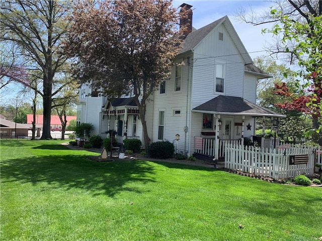 view of front facade with covered porch, a chimney, a shingled roof, and a front yard