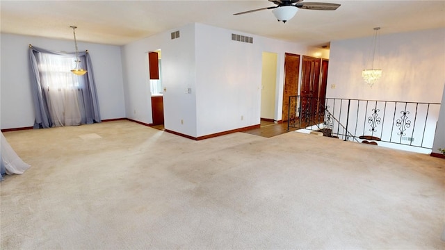 carpeted spare room featuring ceiling fan with notable chandelier