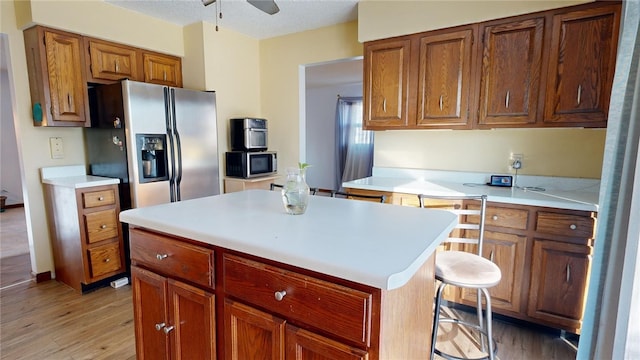 kitchen with appliances with stainless steel finishes, a center island, light hardwood / wood-style floors, ceiling fan, and a breakfast bar