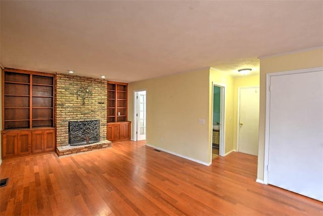 unfurnished living room featuring light wood-type flooring, a fireplace, and built in shelves