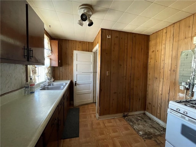 kitchen featuring a sink, wooden walls, light countertops, baseboards, and white gas range