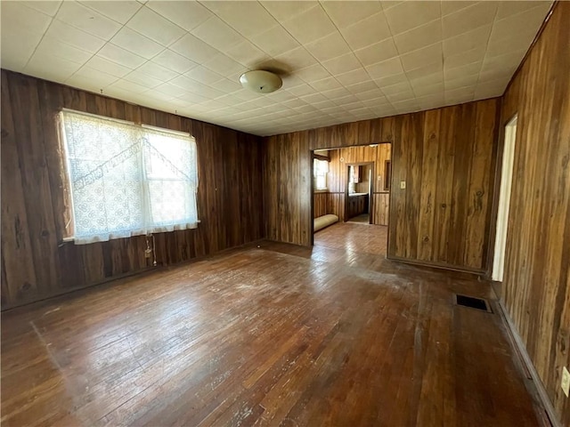 empty room with visible vents, wood walls, and wood-type flooring