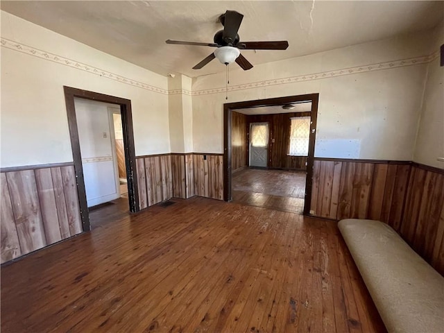 empty room featuring wooden walls, ceiling fan, wainscoting, and hardwood / wood-style flooring