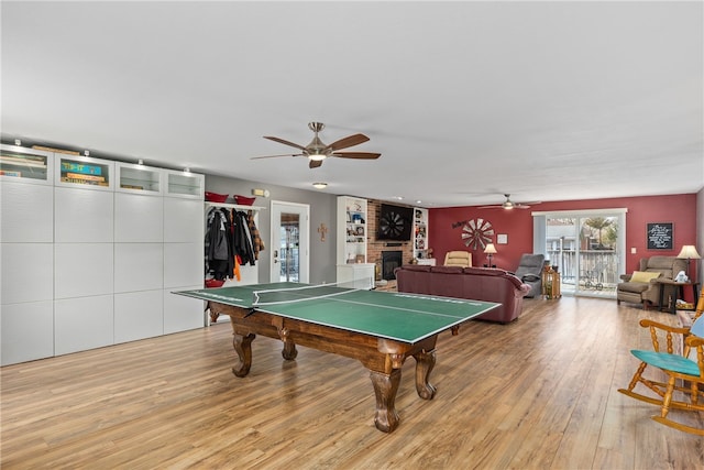 recreation room featuring a brick fireplace, light hardwood / wood-style flooring, and ceiling fan