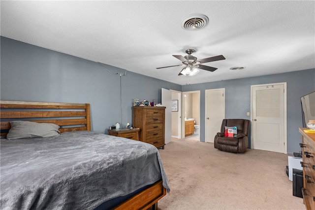 bedroom featuring ceiling fan, ensuite bathroom, light colored carpet, and a textured ceiling