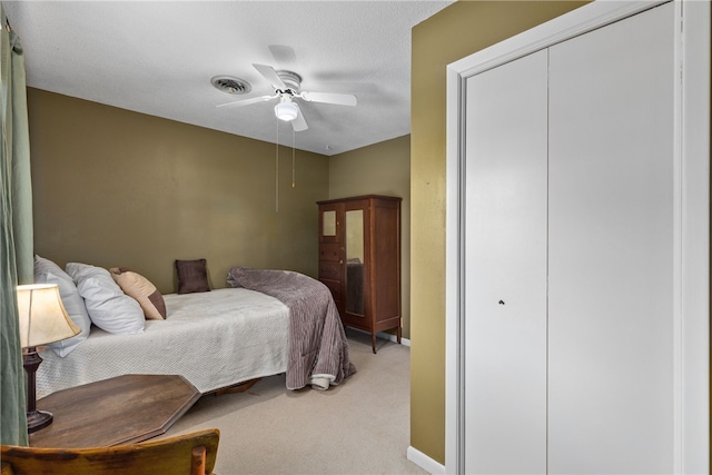 bedroom featuring ceiling fan, light colored carpet, and a textured ceiling