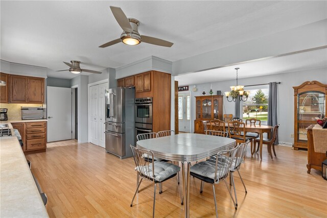 kitchen featuring wall chimney exhaust hood, ceiling fan, light wood-type flooring, tasteful backsplash, and stainless steel appliances