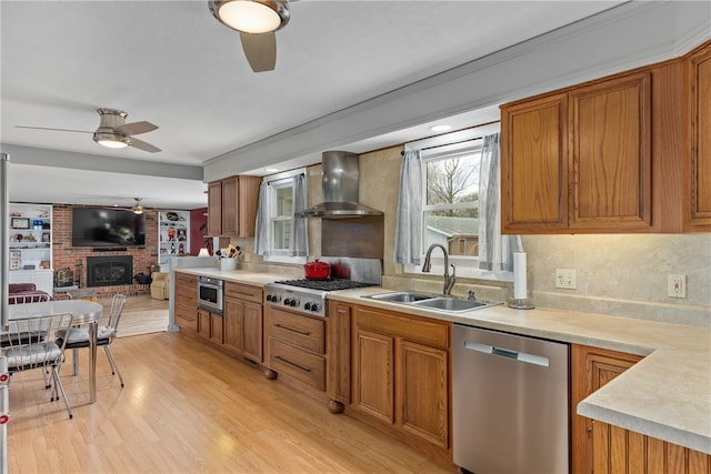 kitchen featuring sink, wall chimney exhaust hood, stainless steel appliances, light hardwood / wood-style flooring, and a fireplace