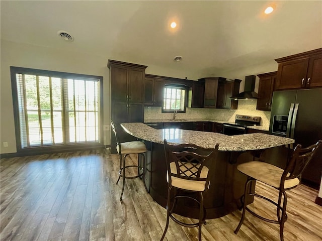 104 Woodland Dr, Marshall, IL 62441 - kitchen featuring backsplash, wall chimney range hood, a breakfast bar area, light wood-type flooring, and stainless steel appliances