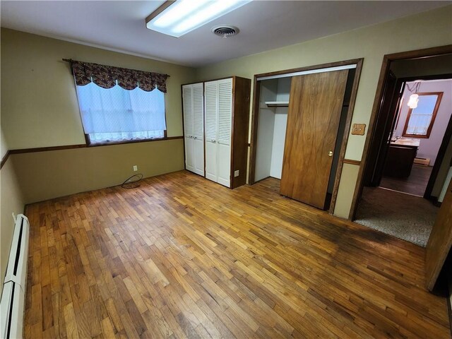 2638 E 1050th Ave, Oblong, IL 62449 - unfurnished bedroom with a baseboard heating unit, hardwood / wood-style floors, and multiple closets