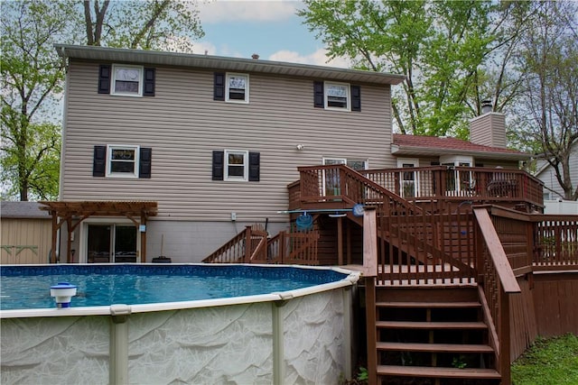 back of property featuring a chimney, a wooden deck, an outdoor pool, stairway, and a pergola