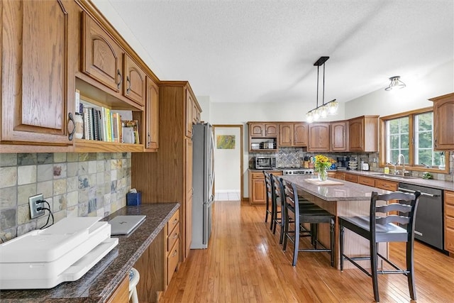 715 W Coolidge Ave, Charleston, IL 61920 - kitchen featuring appliances with stainless steel finishes, backsplash, a breakfast bar, brown cabinetry, and a textured ceiling