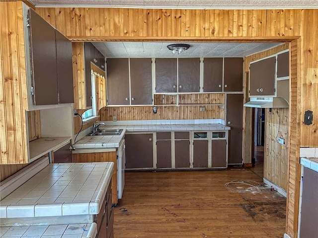 kitchen with dark wood finished floors, wood walls, a sink, and tile counters