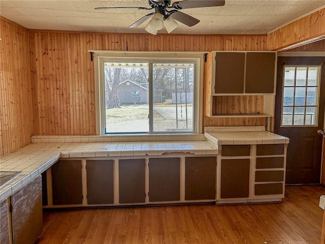 kitchen featuring tile countertops, wood walls, ceiling fan, and wood finished floors