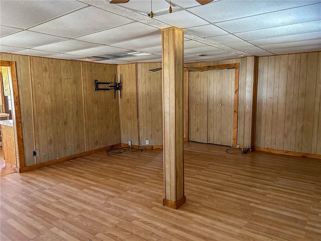 finished basement with wooden walls, a drop ceiling, and wood finished floors