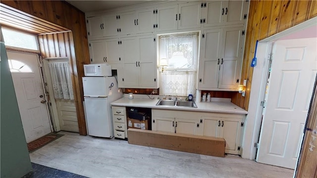 kitchen featuring white cabinetry, wooden walls, sink, and white appliances