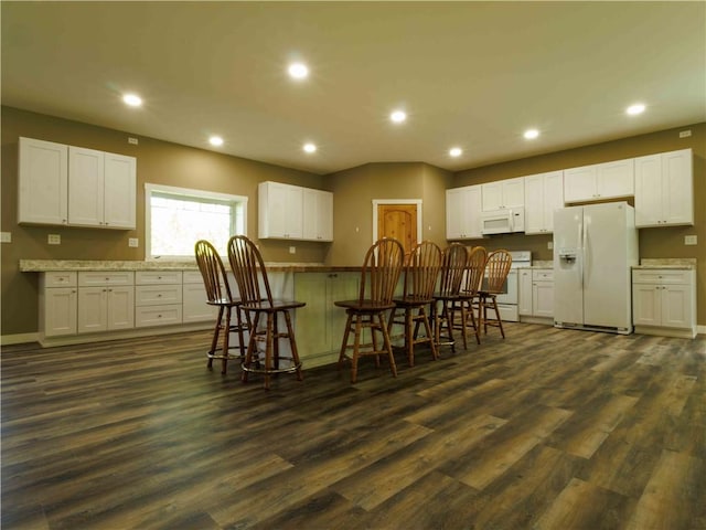 kitchen featuring white appliances, recessed lighting, dark wood finished floors, a kitchen bar, and white cabinets