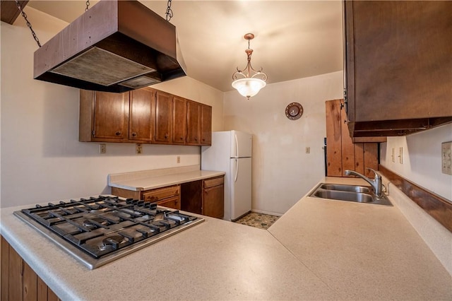 kitchen with extractor fan, freestanding refrigerator, stainless steel gas stovetop, brown cabinetry, and a sink