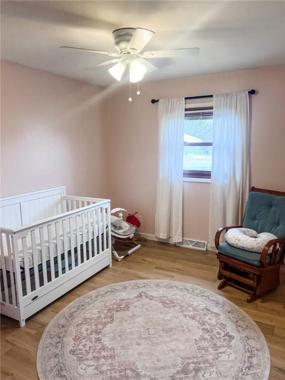 bedroom featuring a nursery area, visible vents, ceiling fan, and wood finished floors