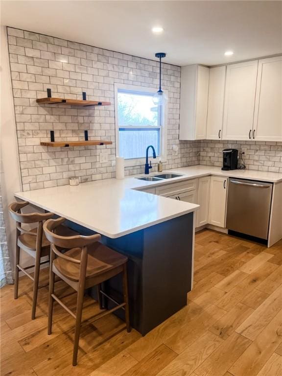 kitchen with light wood-type flooring, stainless steel dishwasher, white cabinets, and a sink