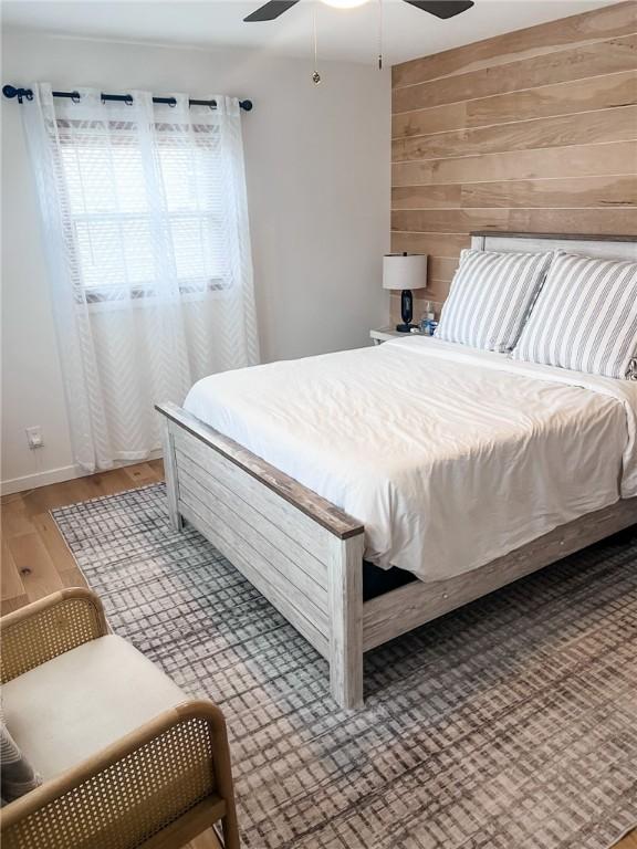 bedroom with ceiling fan, wooden walls, and wood finished floors