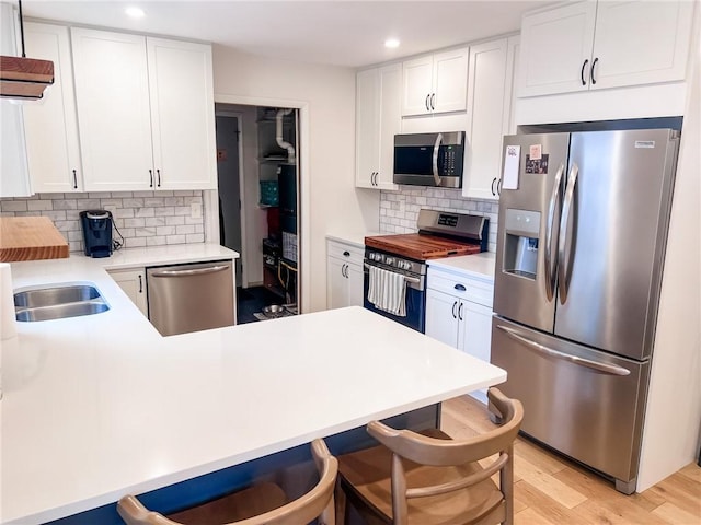 kitchen with appliances with stainless steel finishes, a kitchen breakfast bar, white cabinets, and light wood finished floors