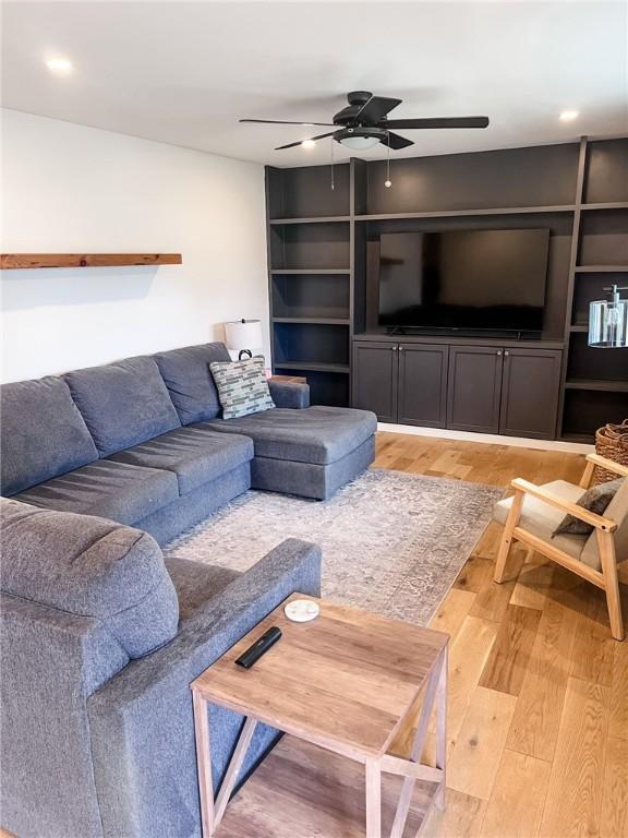 living area featuring a ceiling fan, light wood-style flooring, and built in shelves