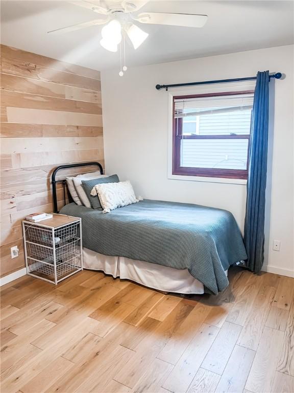 bedroom with light wood-style floors, wood walls, and ceiling fan