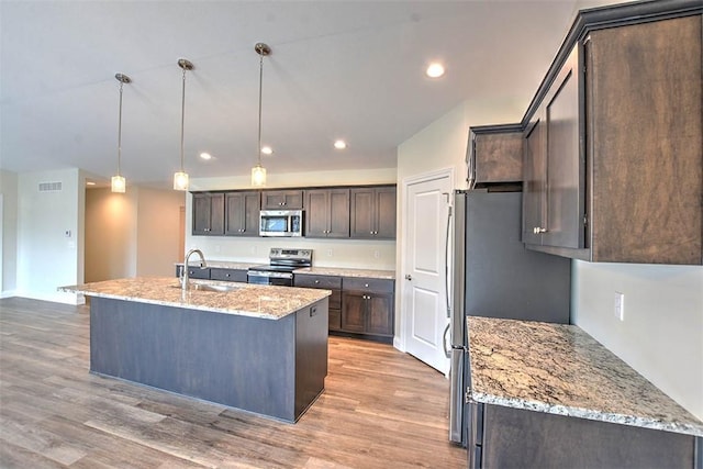 kitchen featuring appliances with stainless steel finishes, light stone counters, decorative light fixtures, light hardwood / wood-style floors, and dark brown cabinetry