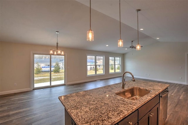 kitchen with a center island with sink, light stone countertops, pendant lighting, sink, and dark hardwood / wood-style floors