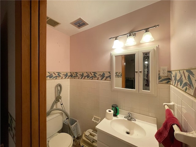 bathroom featuring vanity, tile walls, and toilet