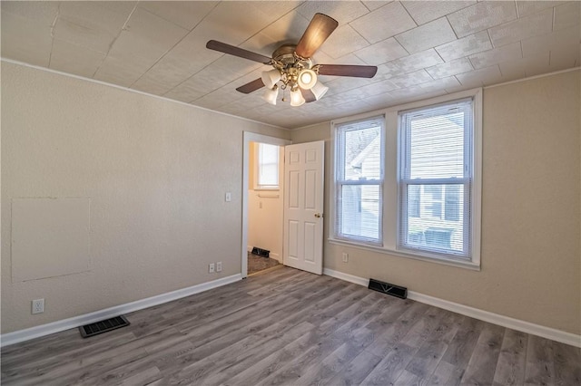 spare room featuring ceiling fan, wood finished floors, visible vents, and baseboards