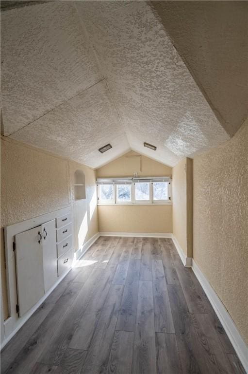 additional living space with baseboards, lofted ceiling, wood finished floors, and a textured wall