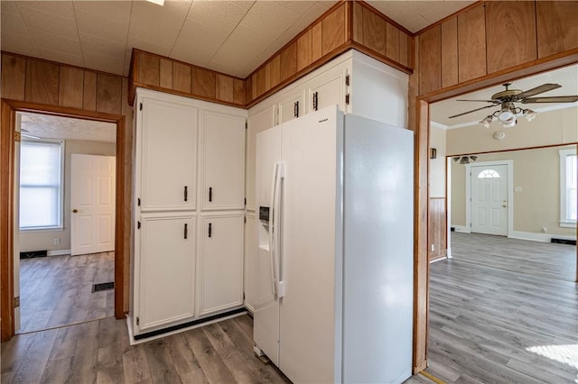 kitchen featuring light wood finished floors, wooden walls, white fridge with ice dispenser, white cabinets, and a ceiling fan