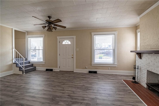 foyer featuring ornamental molding, dark wood-style flooring, a brick fireplace, ceiling fan, and stairs