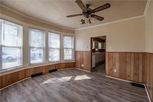 unfurnished room featuring wood finished floors, visible vents, ceiling fan, wood walls, and wainscoting