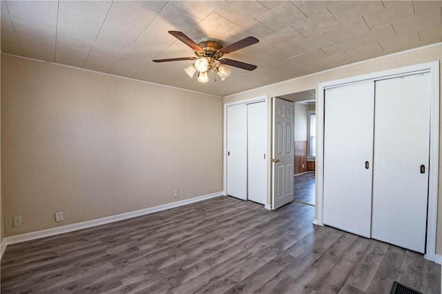 unfurnished bedroom with baseboards, two closets, wood finished floors, and a ceiling fan